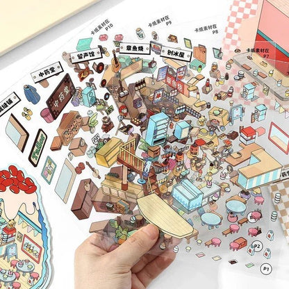 Hand holding clear sheet with colorful city and shop themed scene stickers for journaling or scrapbooking.