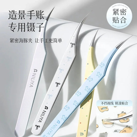 Curved tip tweezers in iridescent blue, white, and yellow with dog and bow designs on a white background.