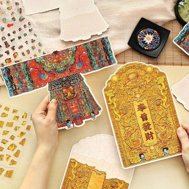 Hands holding vintage-style stickers featuring an ornate imperial silk dance dress and golden dragon-themed plaque with Chinese characters, surrounded by decorative journaling stickers.